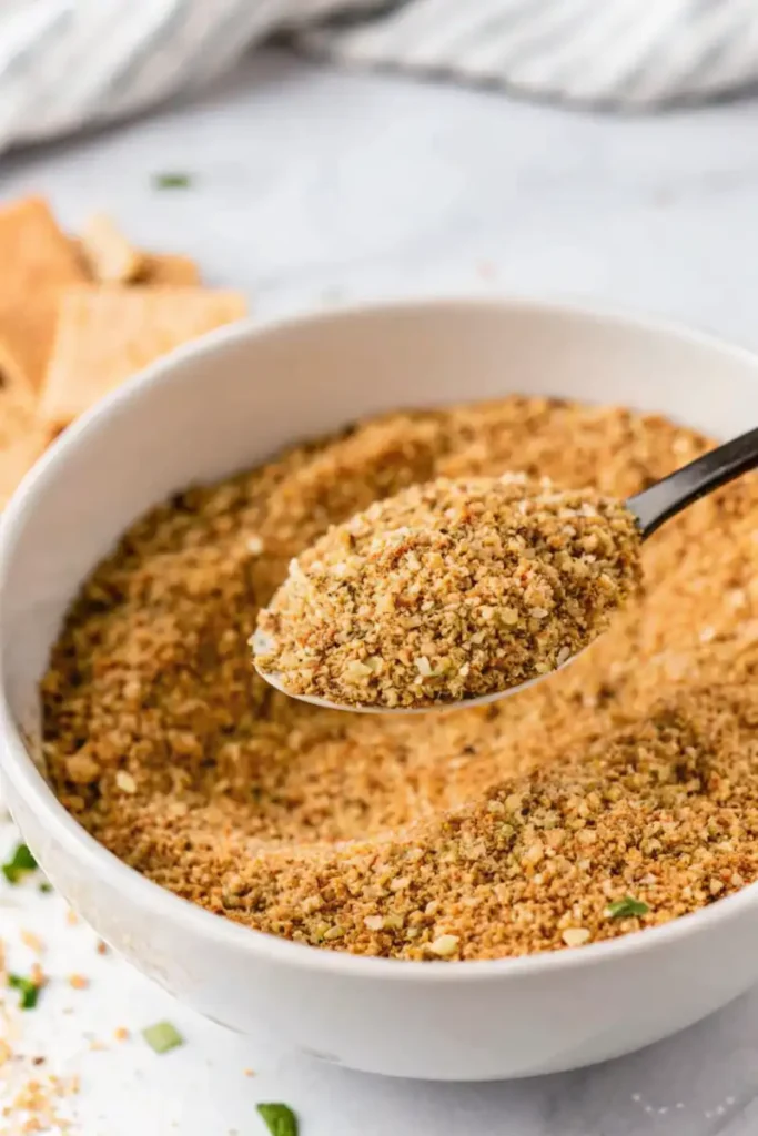 Seasoned gluten-free bread crumbs in a bowl with a spoon.