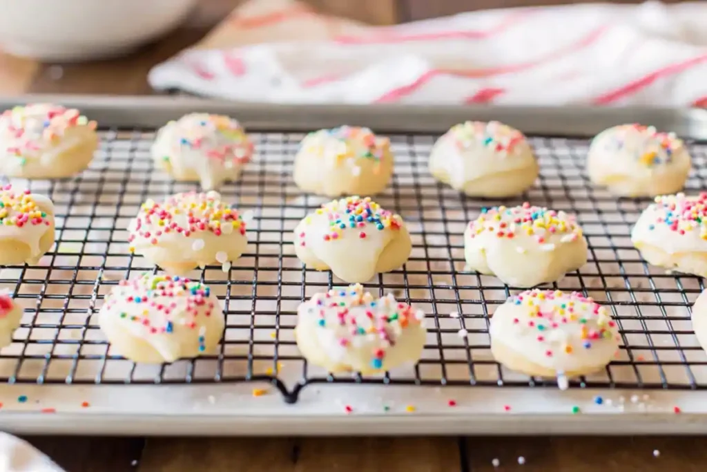 Anise cookies cooling on a wire rack, topped with white glaze and rainbow sprinkles.