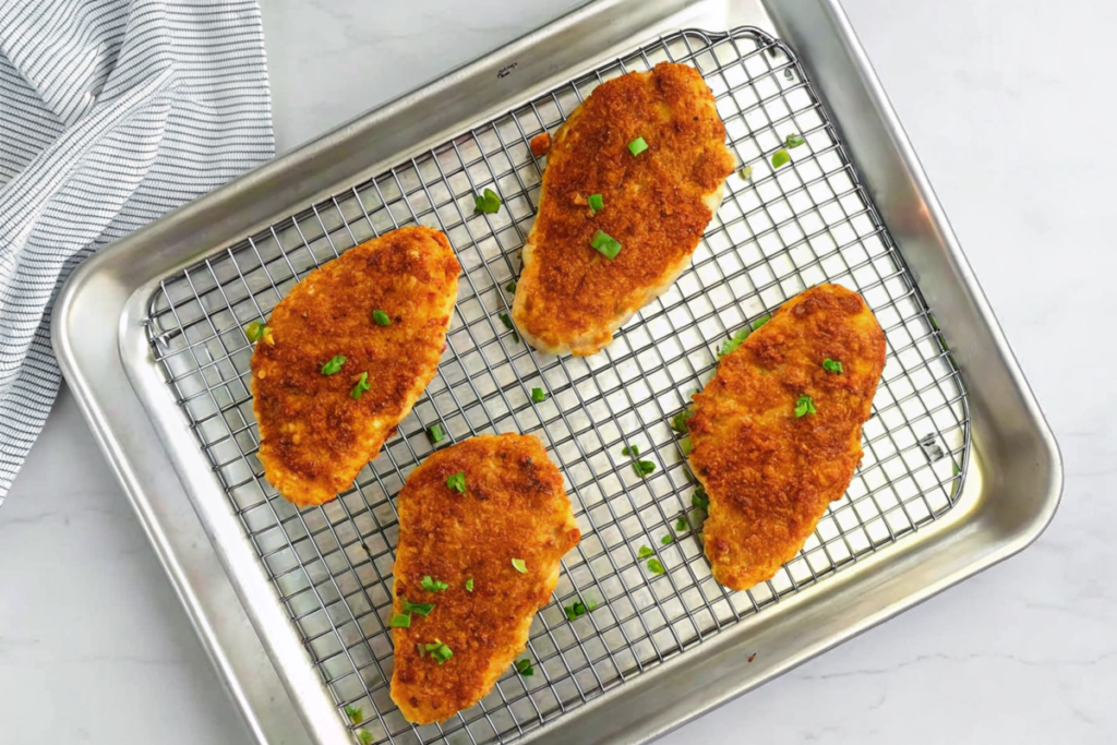 Four panko breaded chicken breasts on a baking rack garnished with parsley