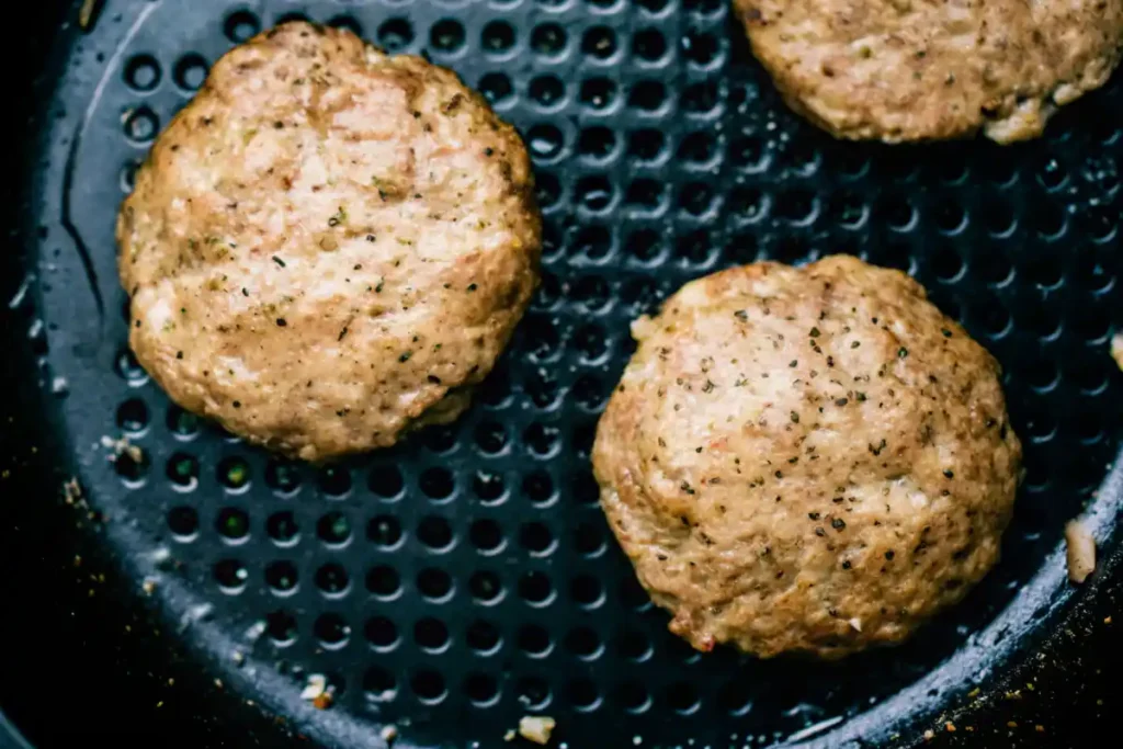 Golden air-fried turkey patties resting inside an air fryer basket, lightly seasoned with herbs.