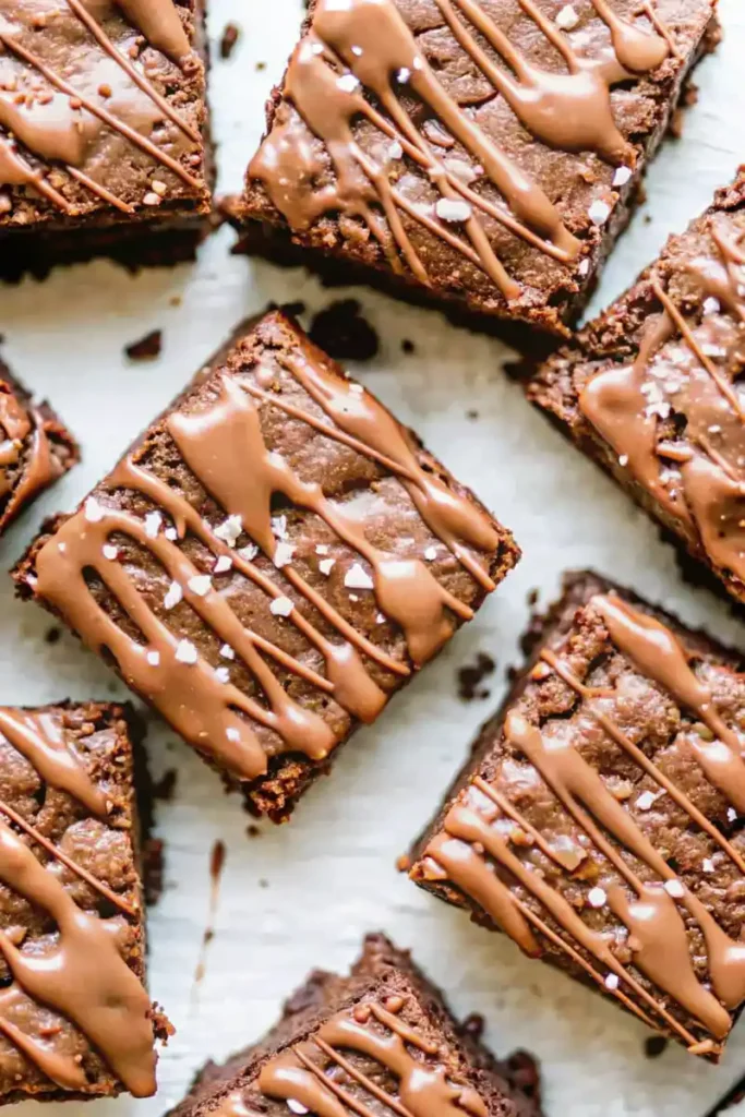 Fudgy protein brownies drizzled with chocolate and sprinkled with sea salt on a white background.