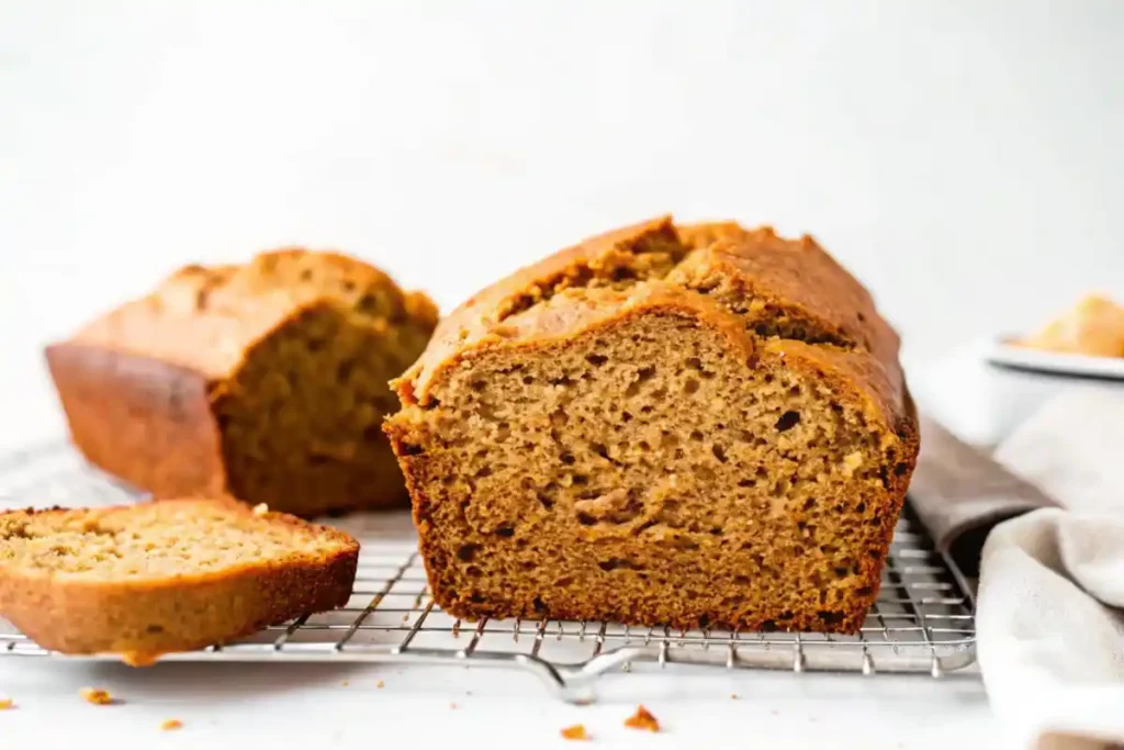 Two loaves of sweet potato bread with one sliced to reveal its moist interior, placed on a wire rack.