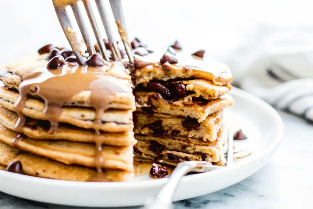 Stack of fluffy protein pancakes topped with chocolate chips and drizzled with peanut butter.