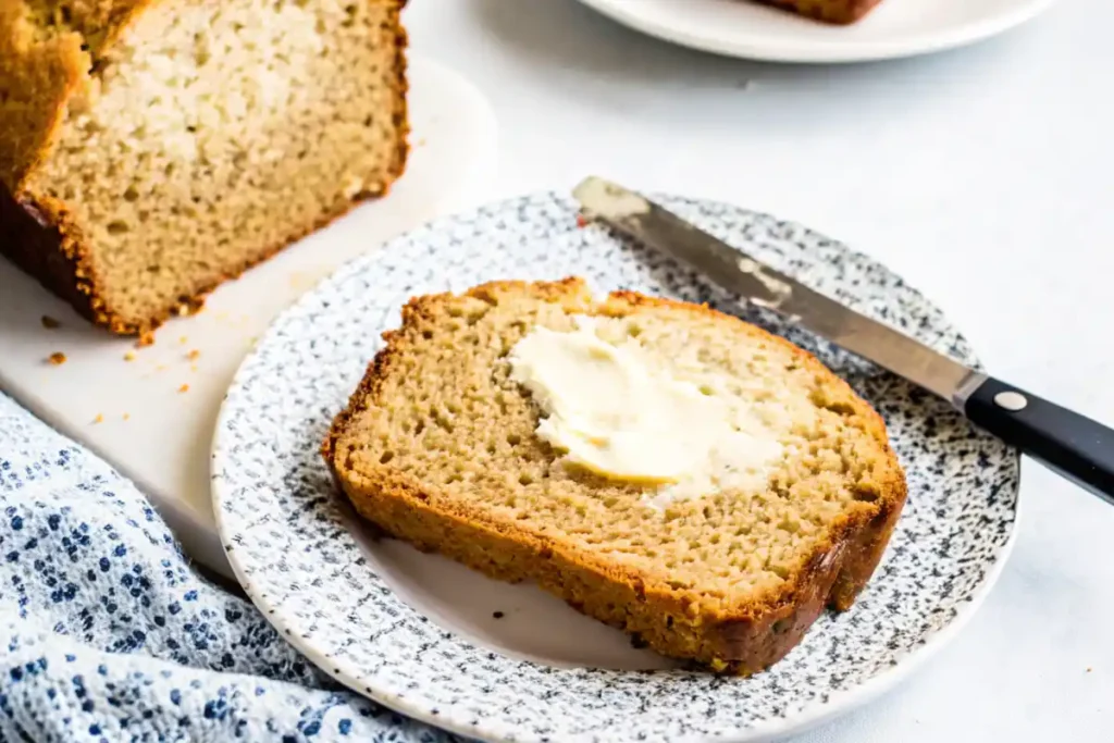 A slice of banana bread on a plate with butter spread on top.