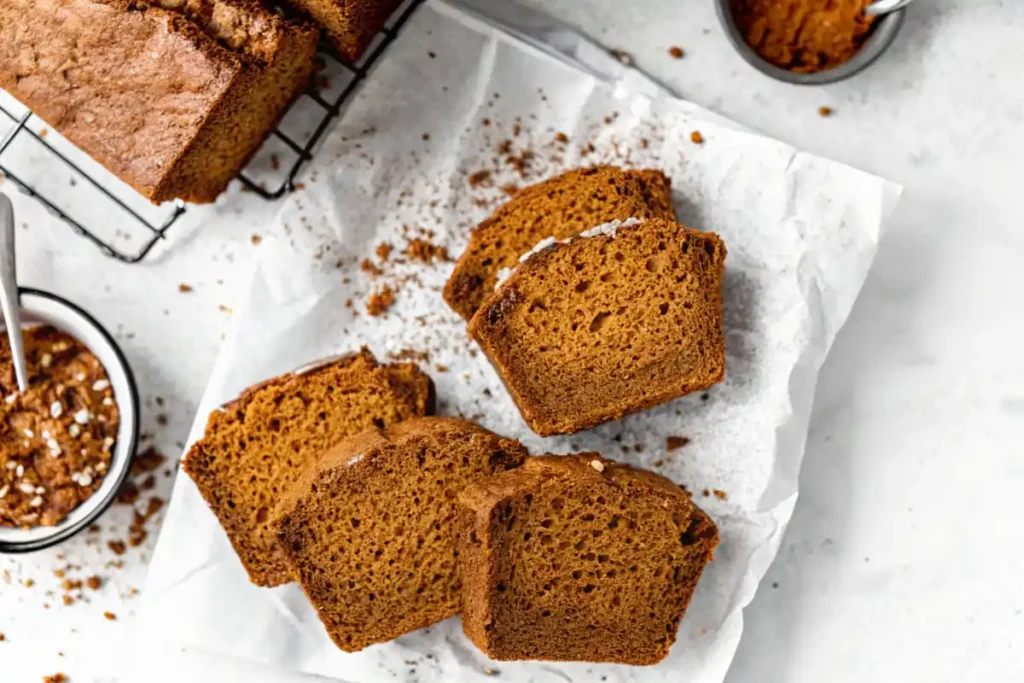 A moist and golden loaf of gluten free pumpkin bread sliced on parchment paper.