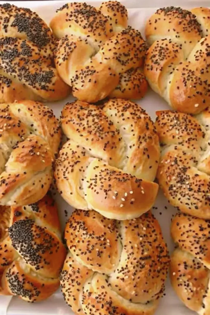 Freshly baked Kaiser rolls topped with poppy seeds on a tray.